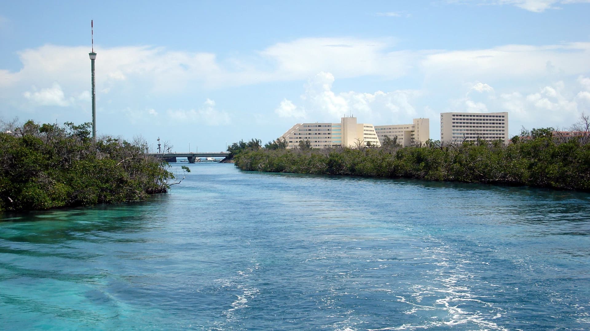 Mangrove-lined channel of the Nichupté Lagoon in Cancún with a boat wake and the hotel zone behind