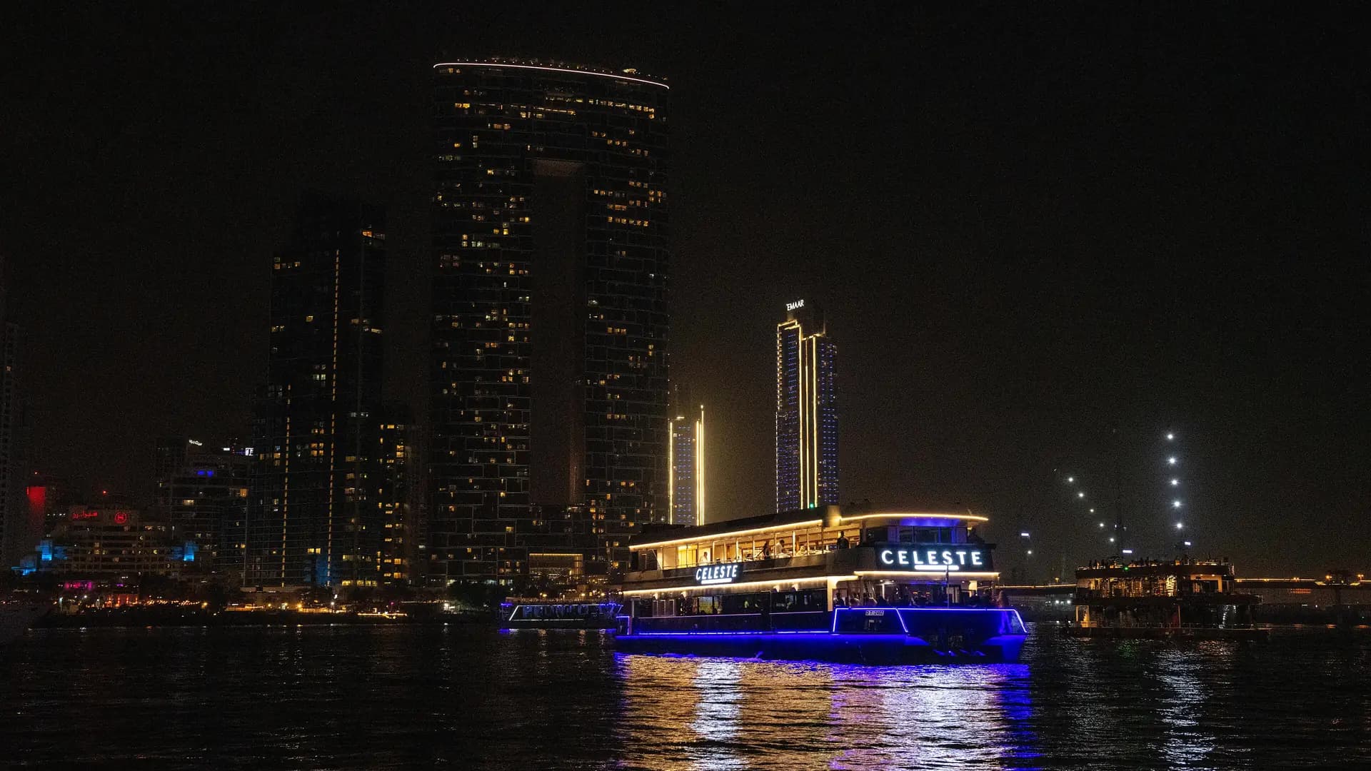 A cruise boat on the water at night with the Dubai skyline behind