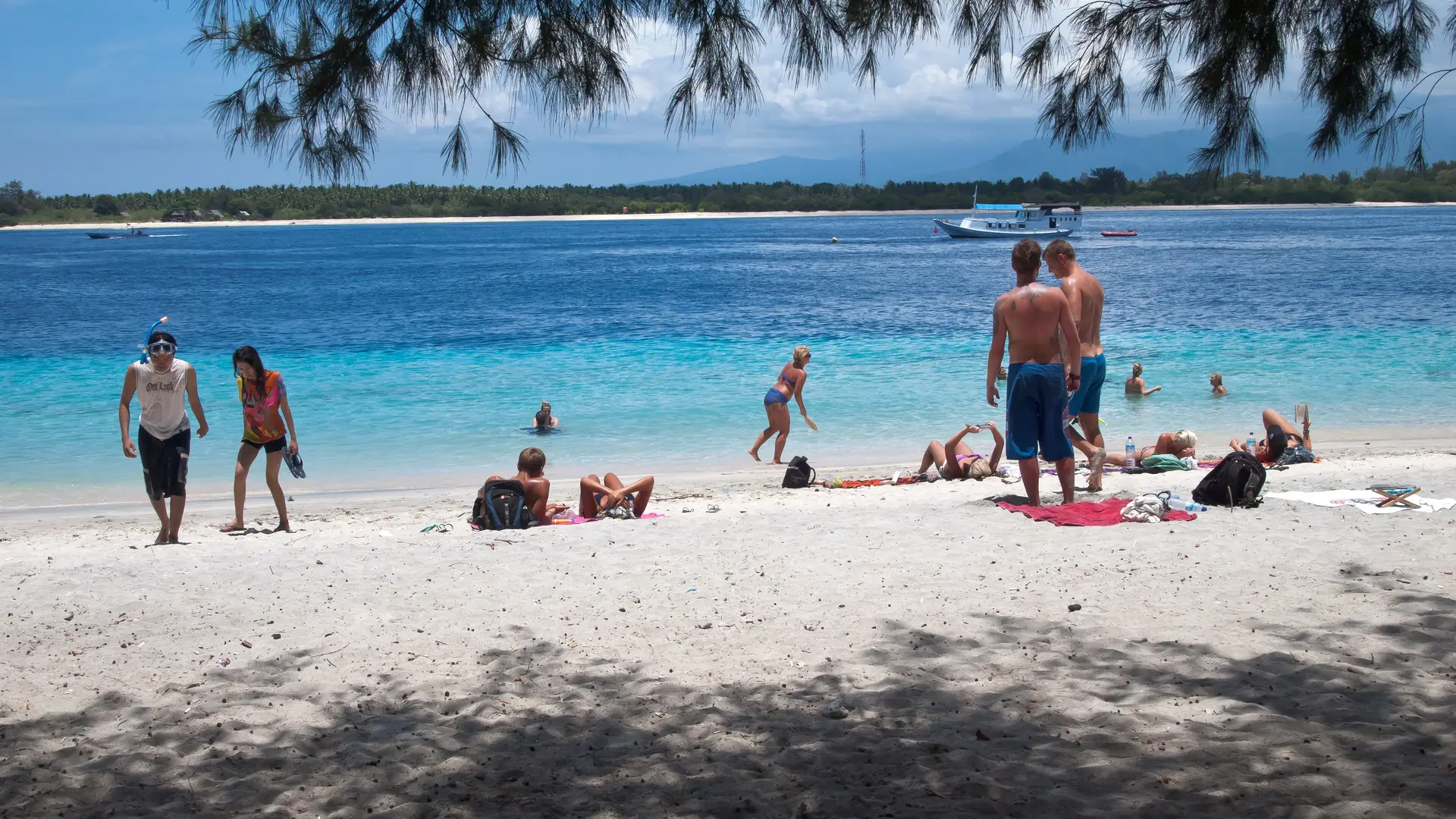 Tourists on the white sand beach of Gili Trawangan, with turquoise water and Lombok's mountains behind