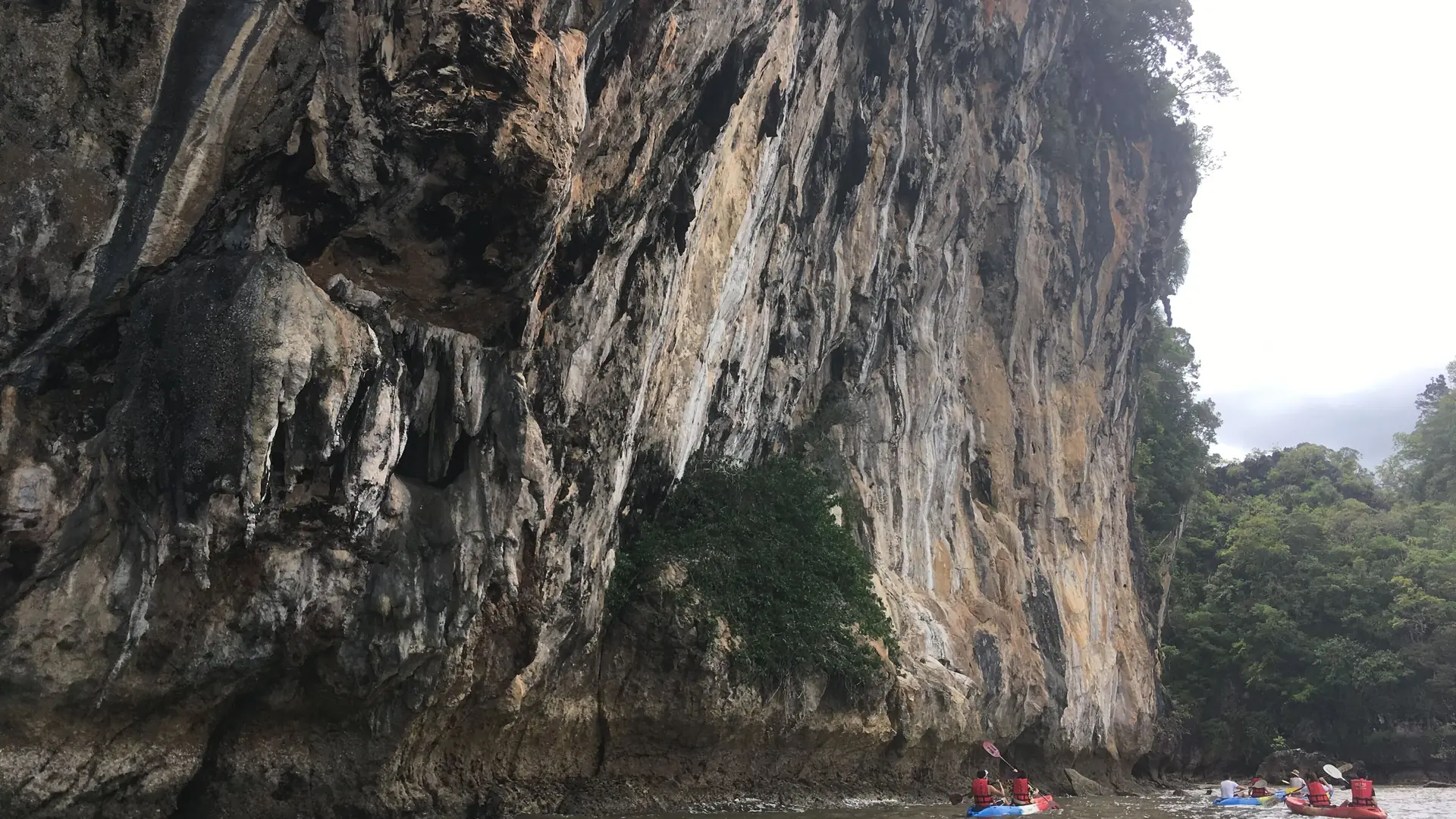 Kayakers paddling below a weathered limestone cliff at Ao Thalane, Krabi, Thailand