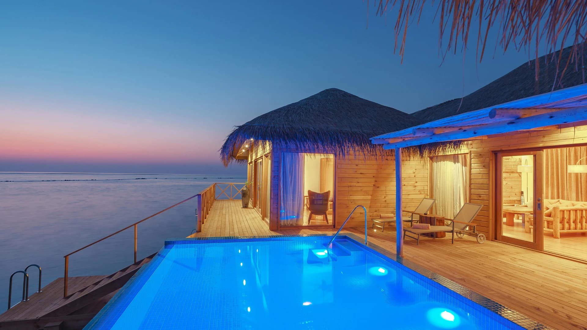 Overwater villa with private pool at sunset over the ocean