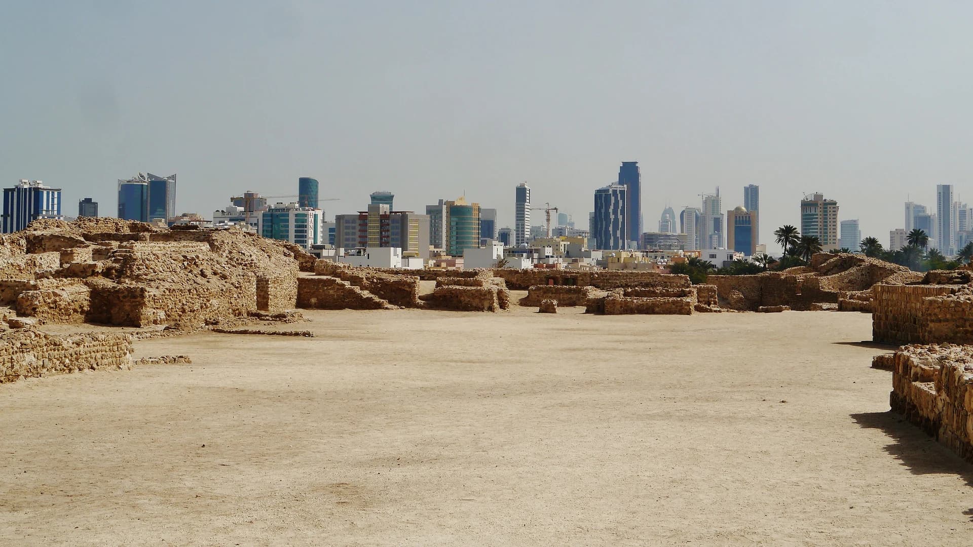 The ancient ruins of Qal'at al-Bahrain fort with the modern Manama skyline behind