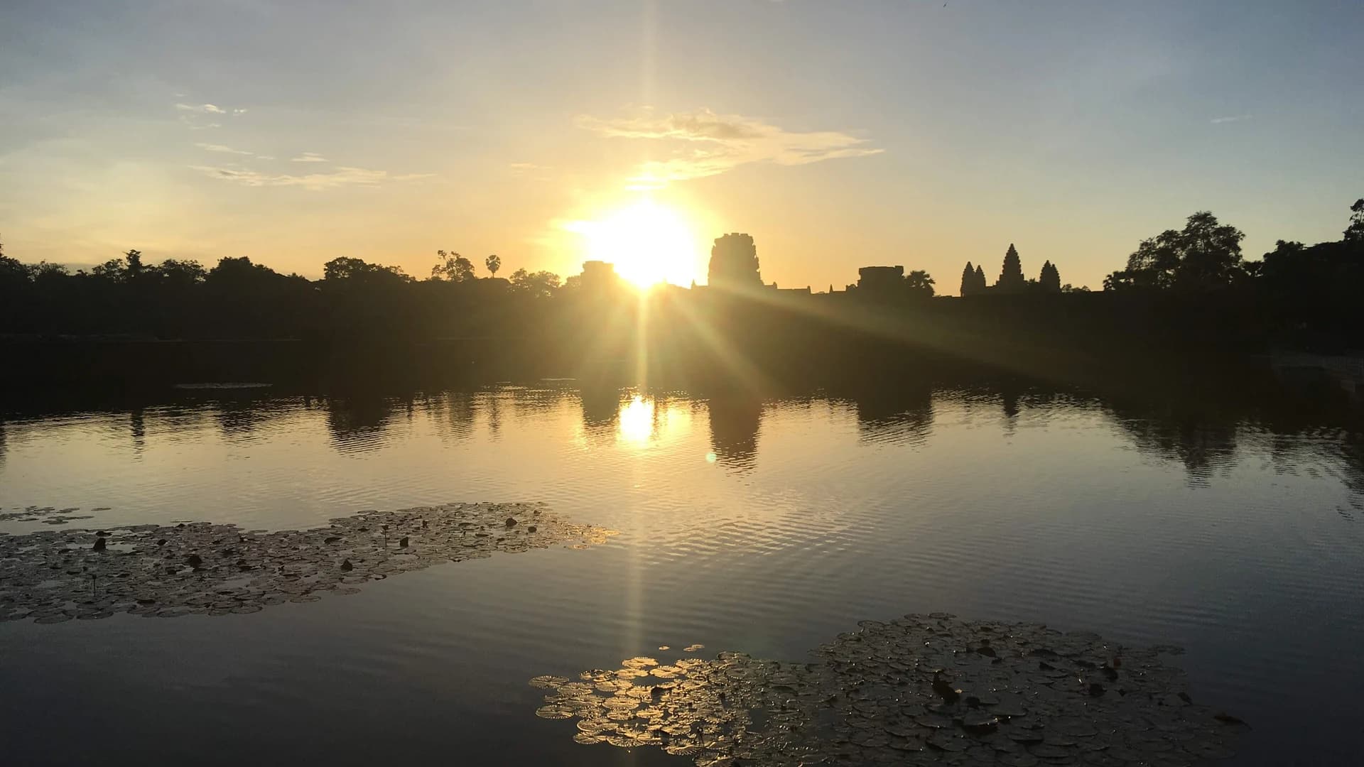 Sunrise silhouette of Angkor Wat's towers reflected in the temple's moat